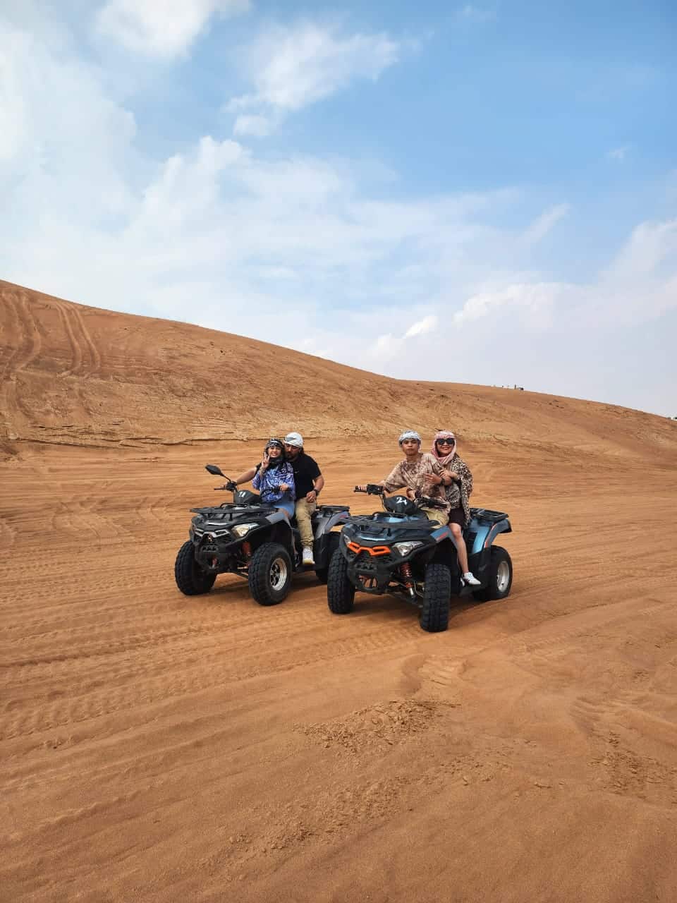 Tourists enjoying quad biking adventure on red dunes in Dubai desert safari.