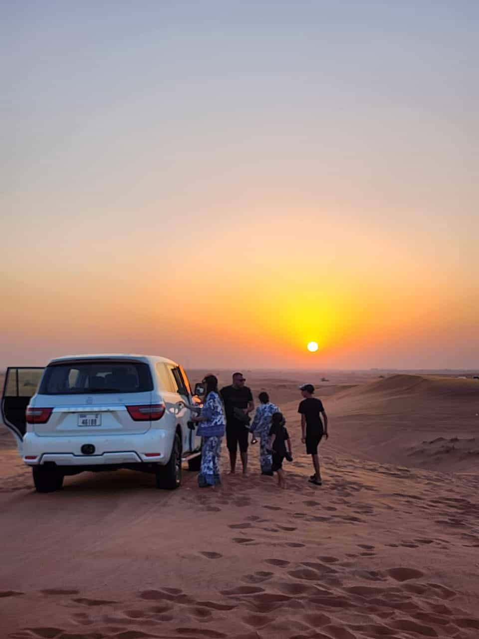 Luxury 4x4 SUV parked on sand dunes during a beautiful sunset in Dubai desert.